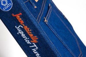 Blue jeans with embroidered text on pocket.