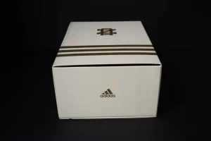 White Adidas shoebox with brown stripes.