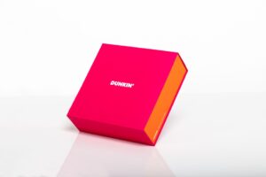 Bright pink Dunkin' box, tilted on surface.